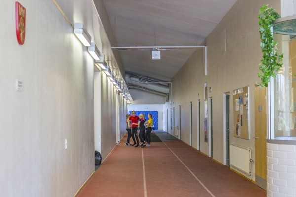 Valaistu urheiluhallin käytävä, jossa joukko nuoria valmistautuu juoksemaan.