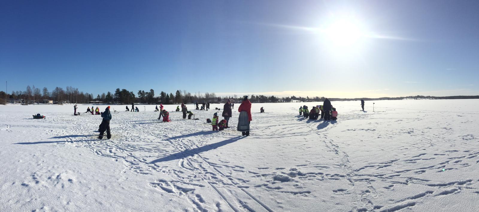 Kuva: Jäätynyt järvi lumen peitossa ja leikkiviä lapsia