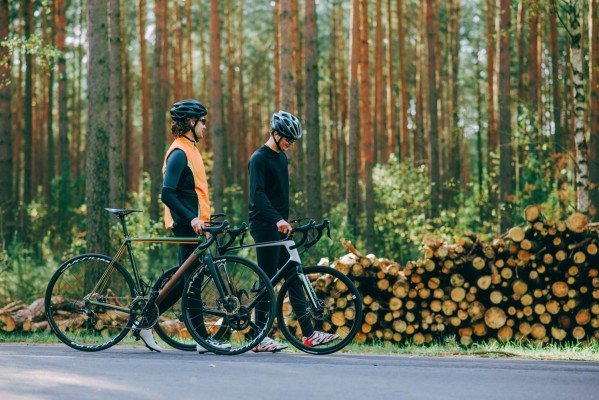 Tre män cyklar på landsväg med skogen i bakgrund.